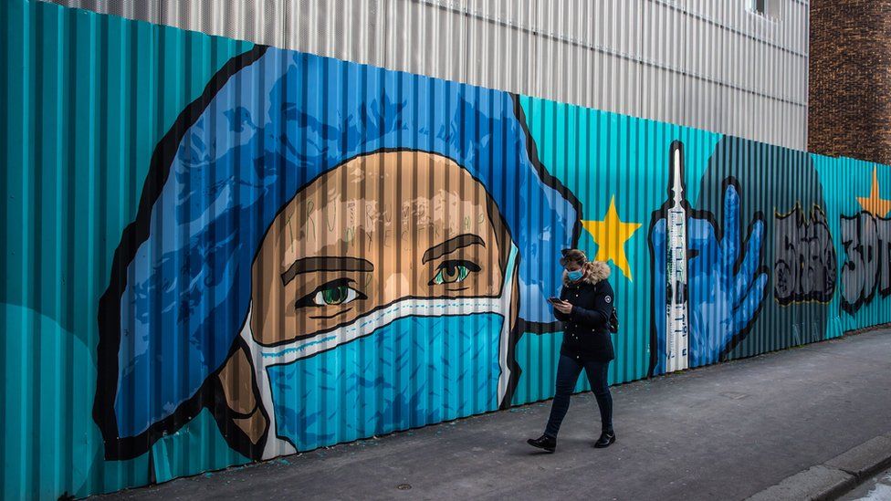 A pedestrian walks past a street-art mural by French artist JBC, in tribute to health workers representing a nurse wearing a protective face mask in front of a hospital in Paris, France, 20 March 2021