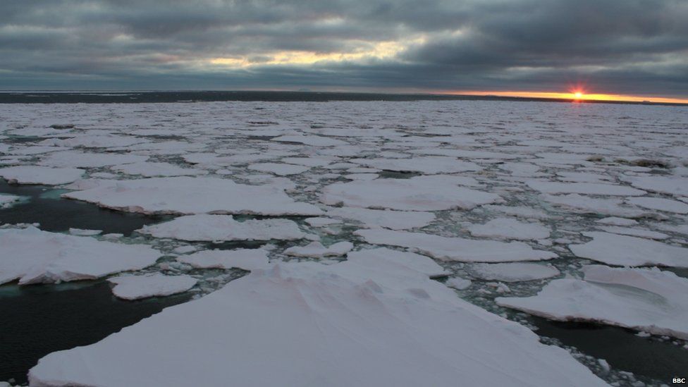 A view over the Weddell Sea, covered in white ice pack. The clouds are low and grey and the sun sets on the horizon