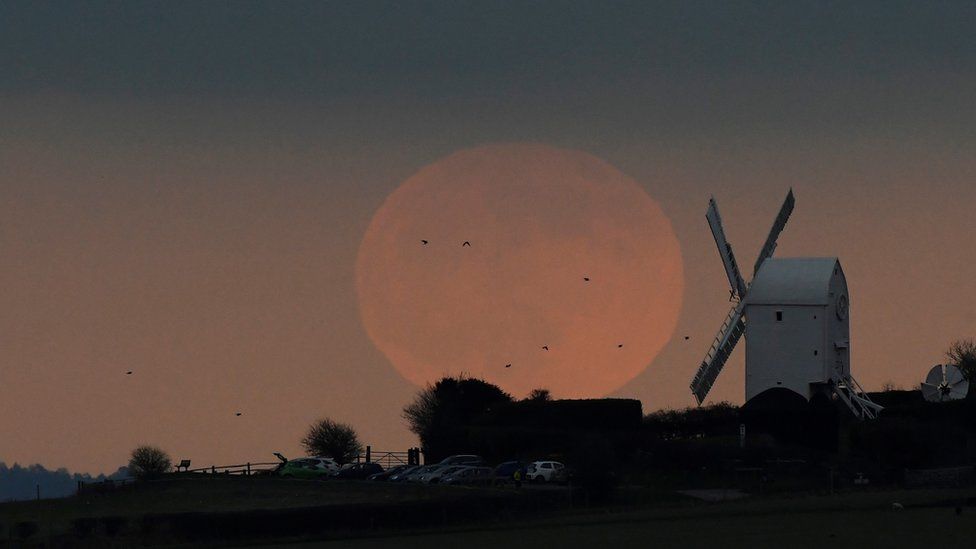 The full moon seen rising behind a windmill on the Sussex downs