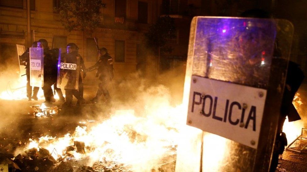 Police officers stand guard amid burning barricades in Barcelona. Photo: 16 October 2019