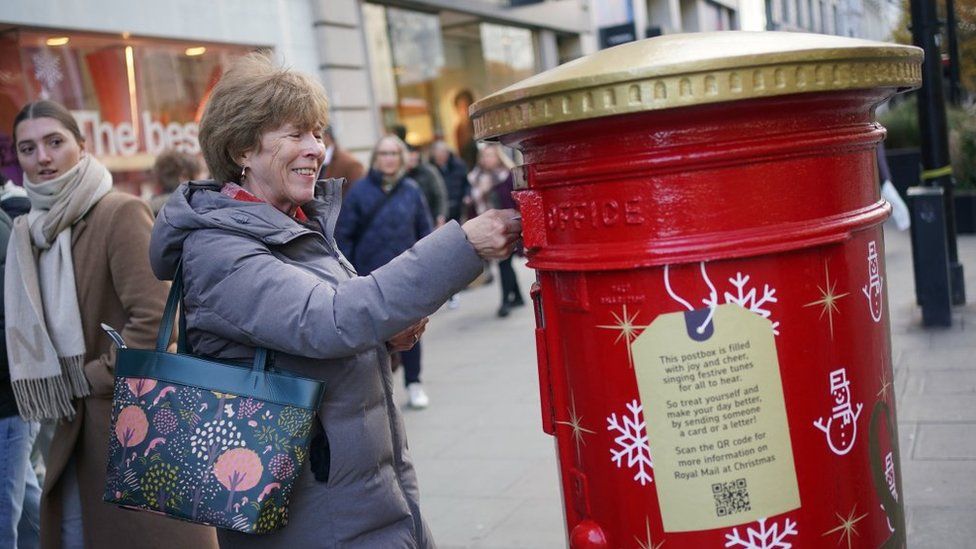 A woman smiles as she is sung a tune by the red and gold postbox on Oxford Street in London