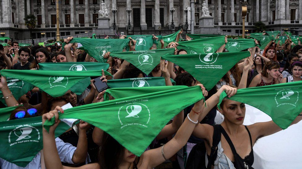 women holding green handkerchiefs above their heads in unison