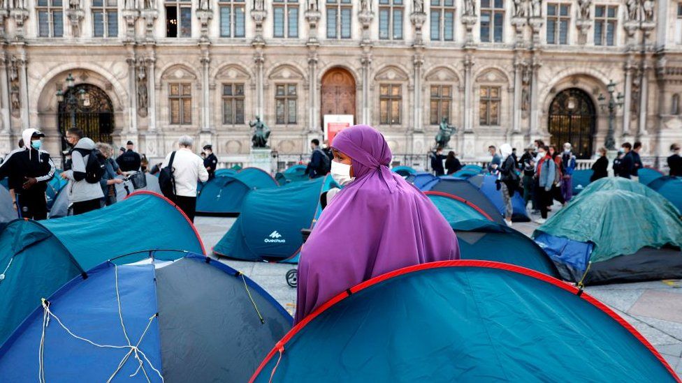 A woman with a mask stands as migrants are evacuated by police in front of the town hall of Paris, on September 1, 2020