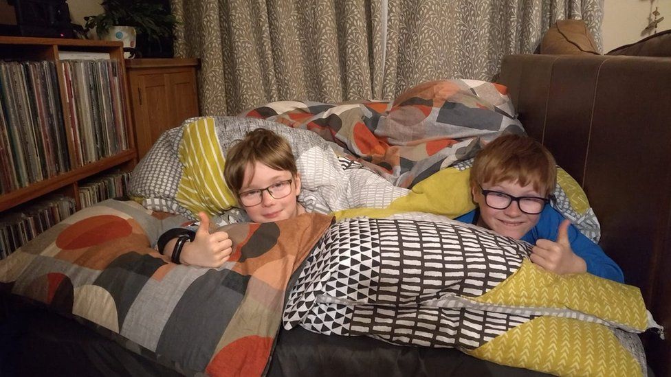 Two boys in duvets on sofa