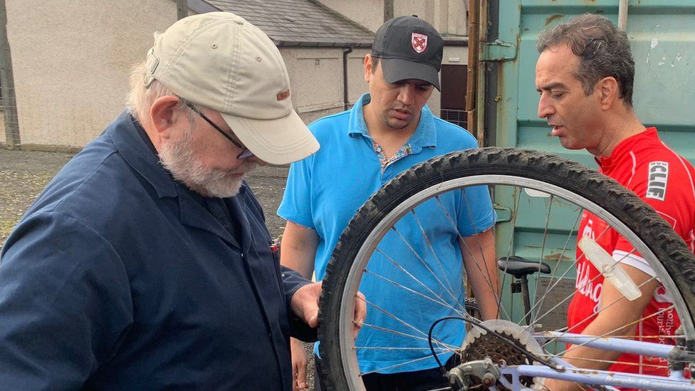 Three men fixing bicycle wheel
