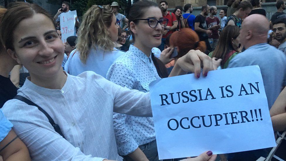 A protester holds up a piece of paper accusing Russia of occupying Georgian lands