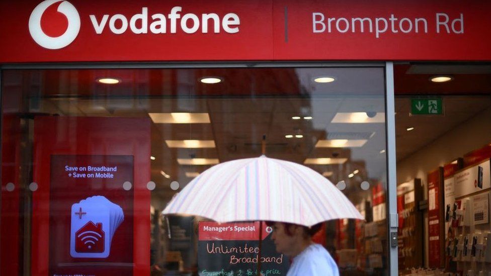 Person with an umbrella successful  beforehand   of a UK Vodafone store.