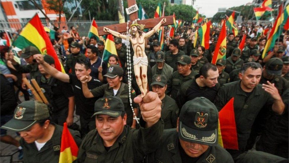 A police officer holds a crucifix among comrades and people taking to the streets of Santa Cruz to celebrate the resignation of Bolivian President Evo Morales on November 10, 2019.