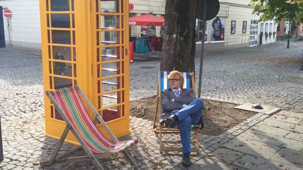 John Byford sitting next to a yellow phone box
