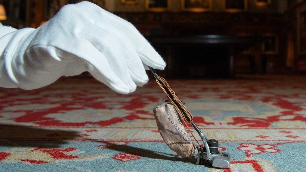 tiny Hoover vacuum cleaner held by white glove