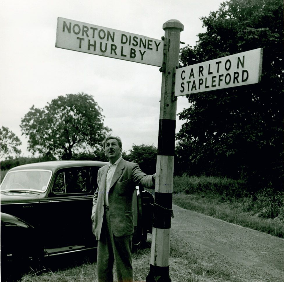 Walt Disney next to a road sign pointing to Norton Disney