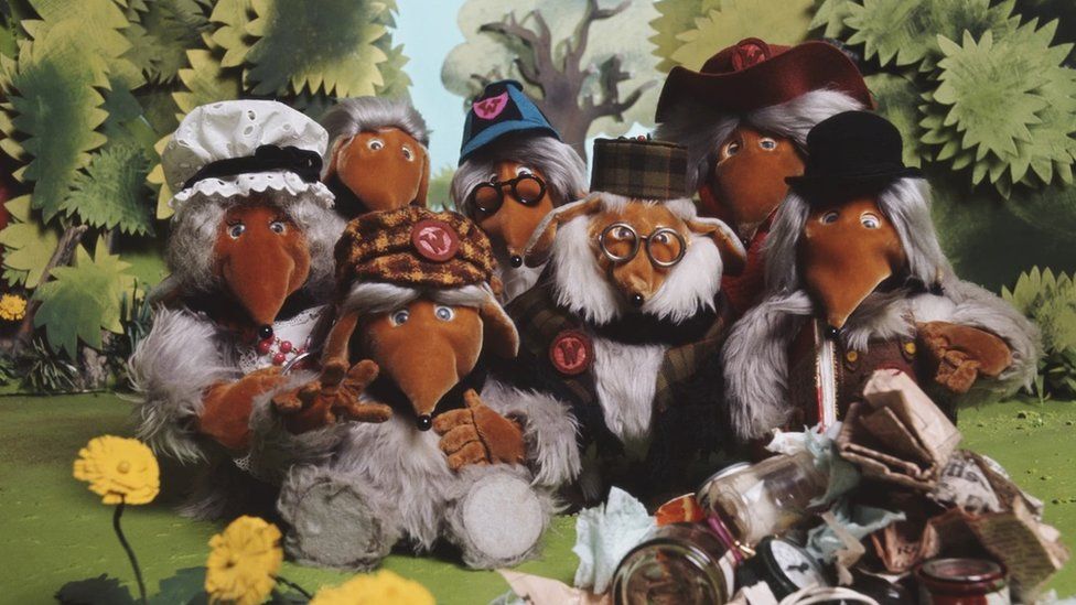 Furry creatures "the Wombles" gather around a pile of rubbish