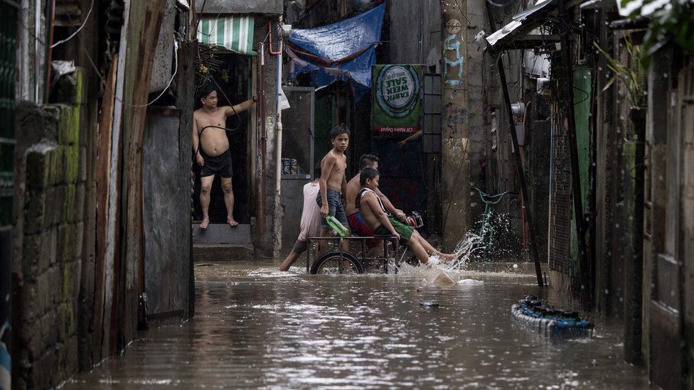Boys ride a rickshaw through a flooded street