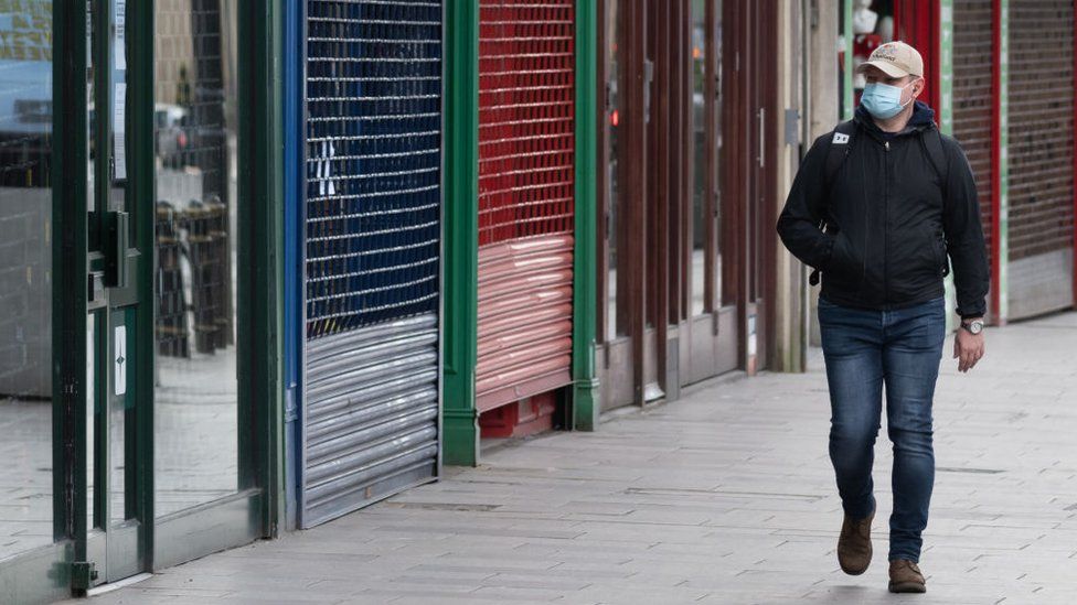 Man in mask walks past empty shops