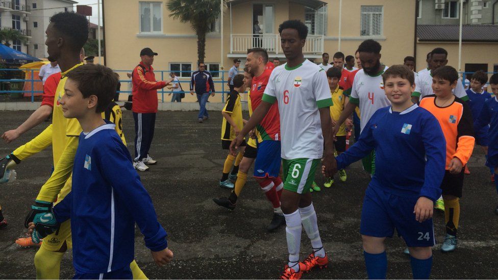 a line of Somaliland footballers being taken on to the pitch by a line of boys