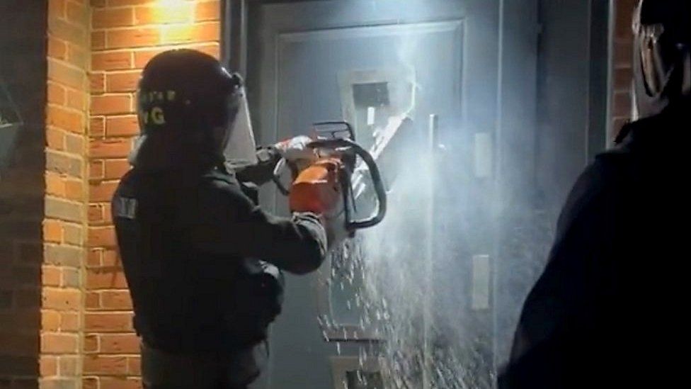 Essex Police use a chainsaw to cut through a door during a raid