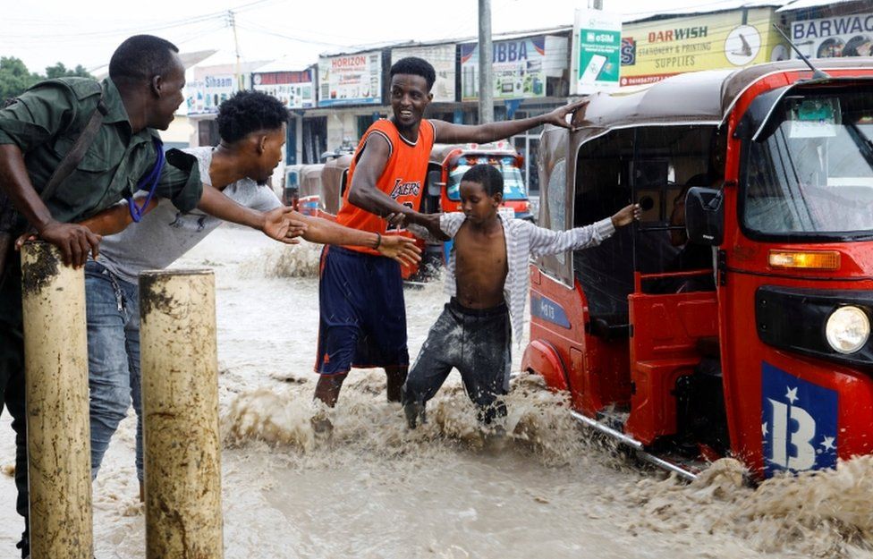 A child is helped as he disembarks from a rickshaw taxi in a flooded road.