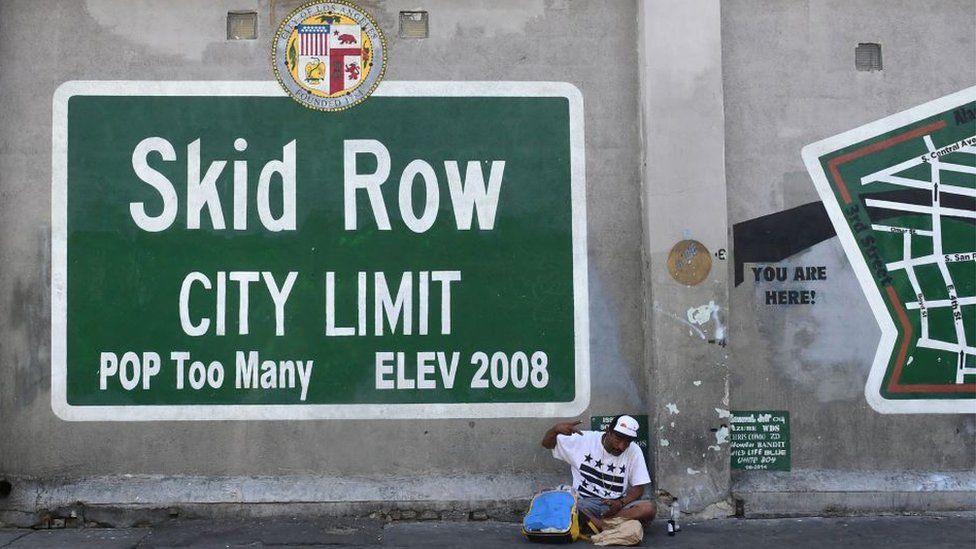 Skid Row sign with man sitting underneath it