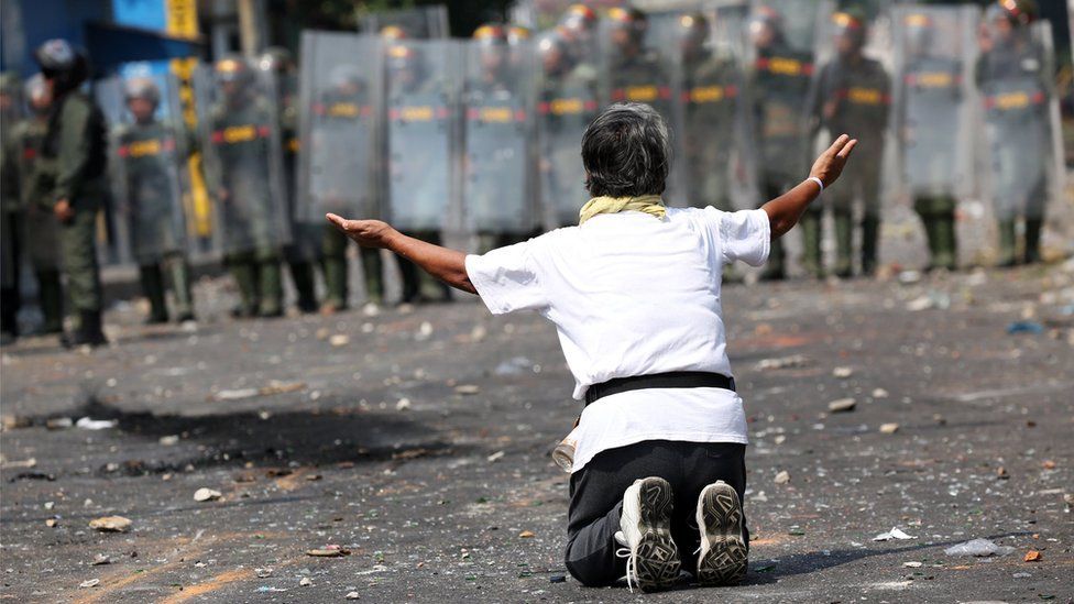 A demonstrator kneels down in front of security forces in Ureña, Venezuela