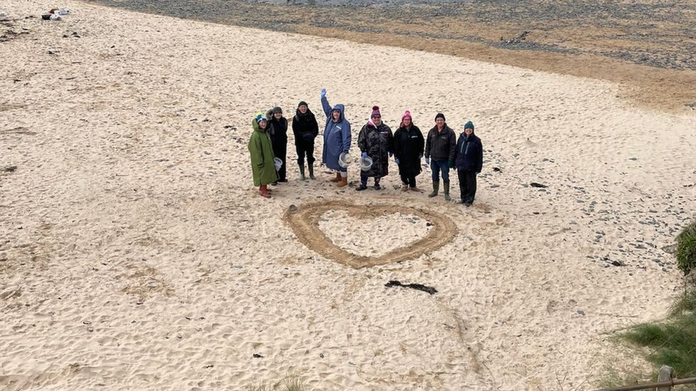 People standing by heart in sand after beach clean at Seven Bays