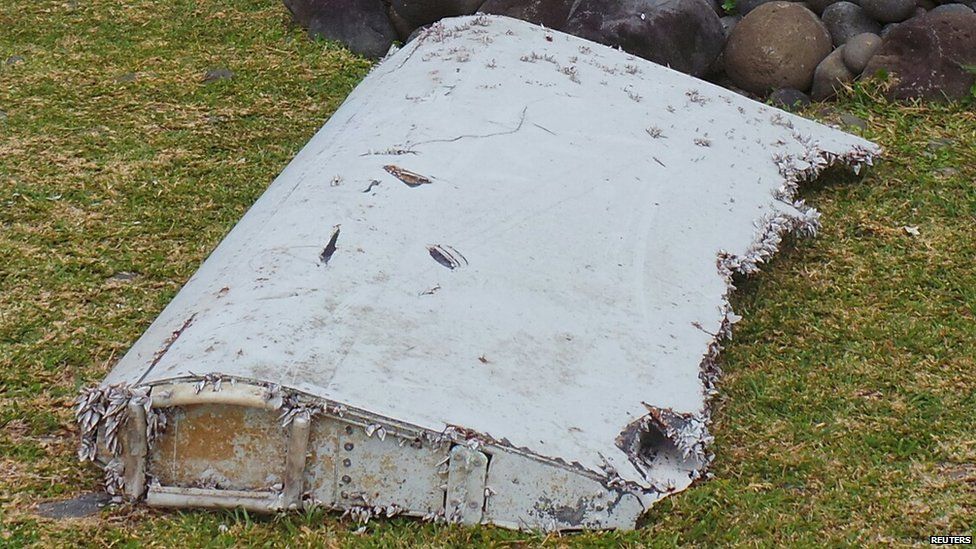 French gendarmes and police stand near a large piece of plane debris which was found on the beach in Saint-Andre, on the French Indian Ocean island of La Reunion, July 29, 2015.