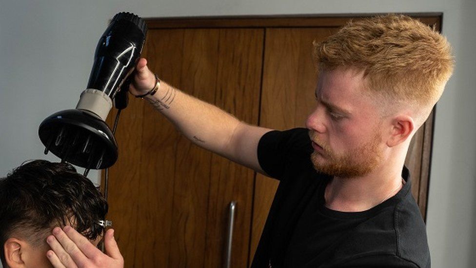 Hairdresser George Smith holds a hairdryer above a models head as he finishes a haircut.