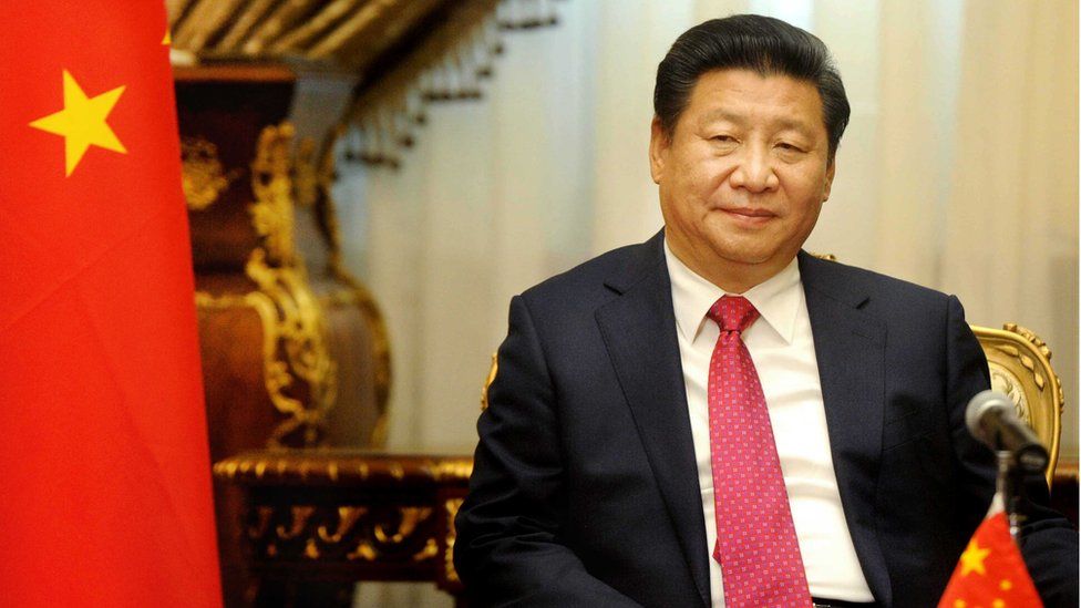 Xi Jinping seated next to a Chinese flag