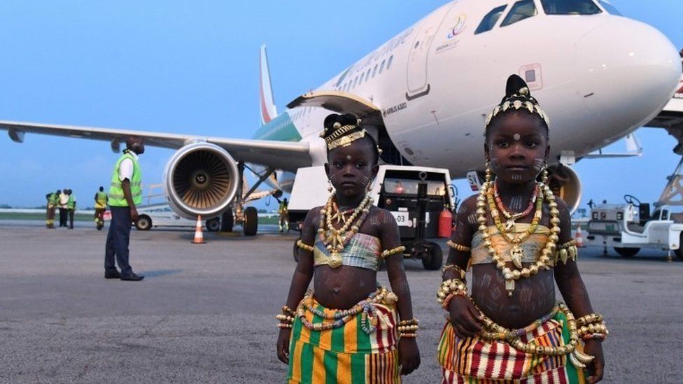 Two young girls in traditional dress pose in front of the tenth airplane of Ivory Coast's national carrier Air Cote d"Ivoire, a new generation Airbus A320, during a ceremony at Felix Houphouet-Boigny airport in Abidjan on July 18, 2017.