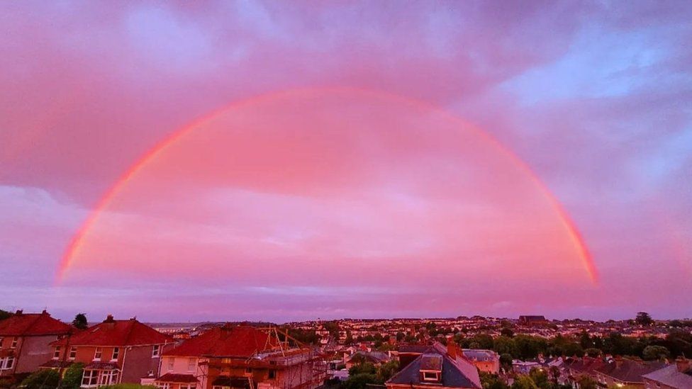 Pink and yellow rainbow above homes in Cornwall