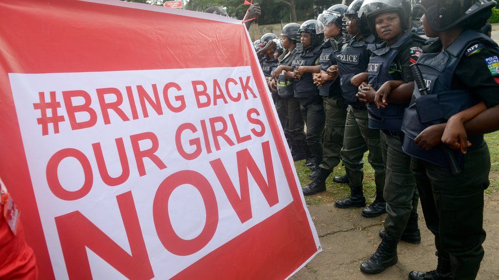 Supporters of the #BringBackOurGirls campaign hold a placard as policewomen block supporters from marching to the president's official residence in Abuja on October 14, 2014.