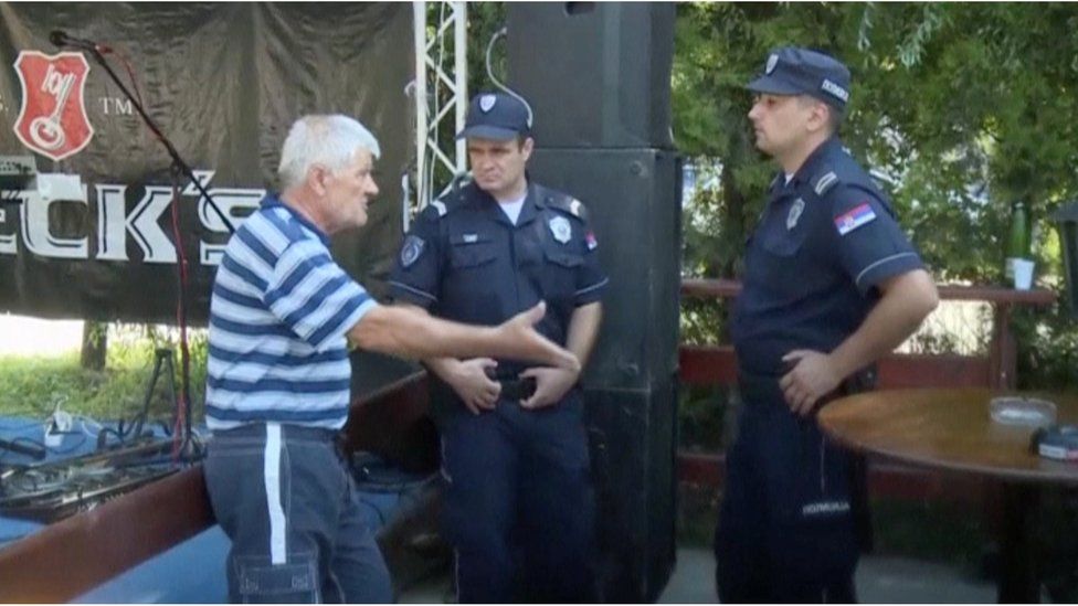 A man talks to police officers at a cafe after a shooting during a local festival in the village of Zitiste, north of Belgrade, Serbia in this still image from video taken 2 July 2016.