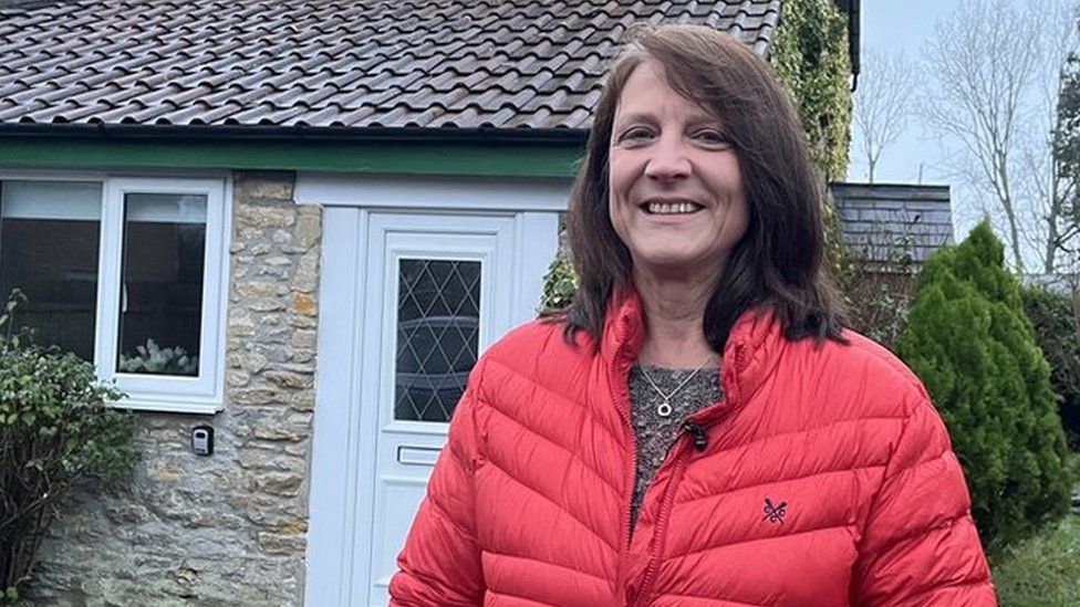 A woman in a red coat outside her rural home