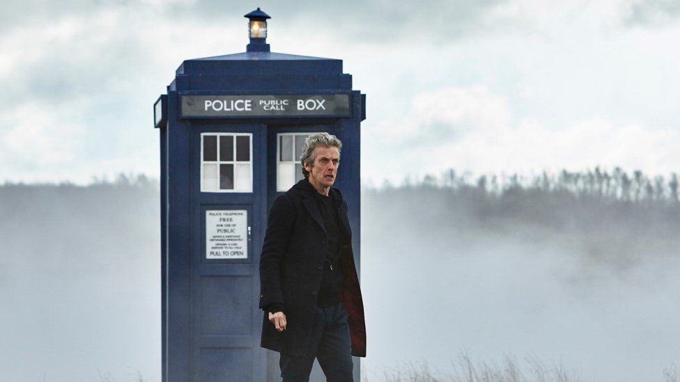 Peter Capaldi as Doctor Who stood in front of the Tardis