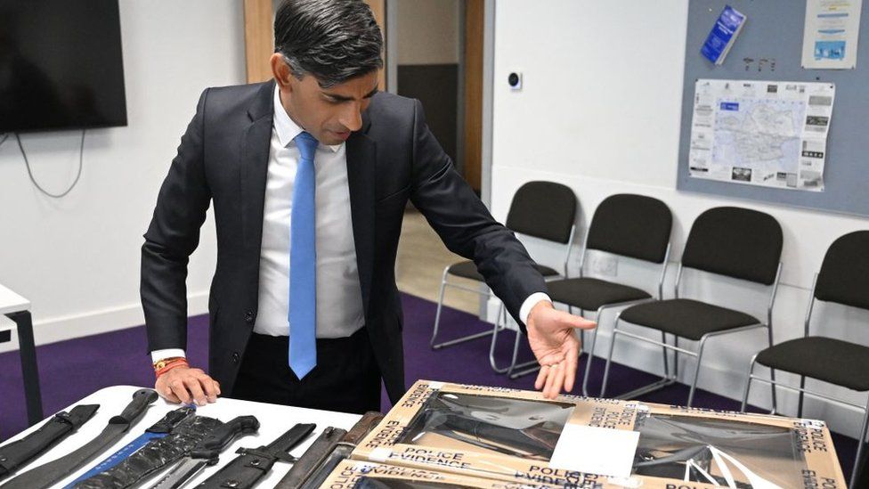 Rishi Sunak looks at knives and machetes seized from knife attacks during a visit to the Kilburn police station