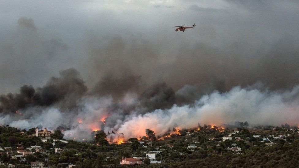 A firefighting helicopter flies over a wildfire raging in the town of Rafina.