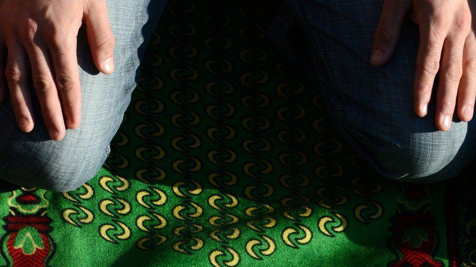A man kneeling on a prayer rug