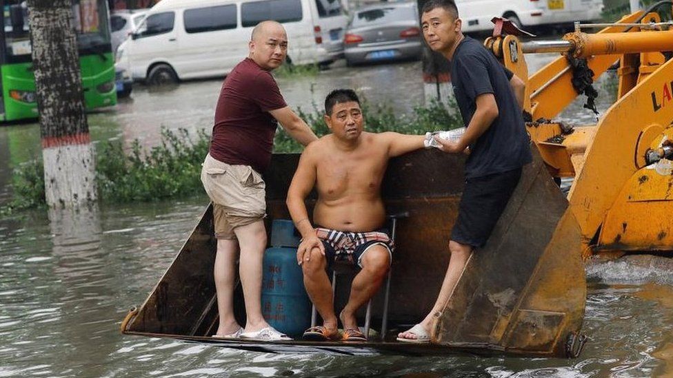 People stand on a front loader travelling through floodwaters after the rains and floods brought by remnants of Typhoon Doksuri, in Zhuozhou, Hebei province, China