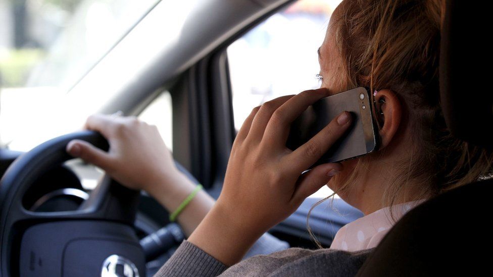 Woman using mobile phone while driving (posed by model)