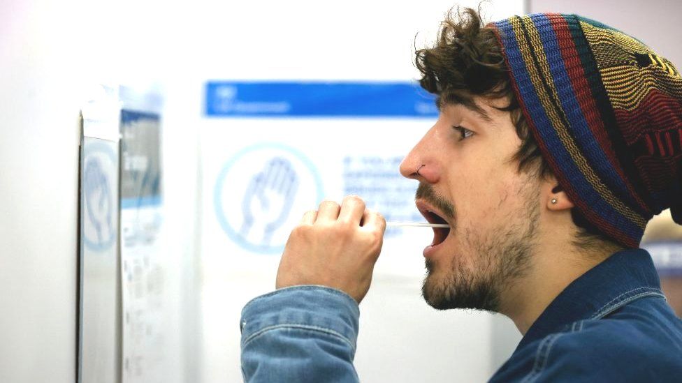 Мужчина использует тампон, чтобы взять образец изо рта в отделении тестирования NHS Test and Trace Covid-19