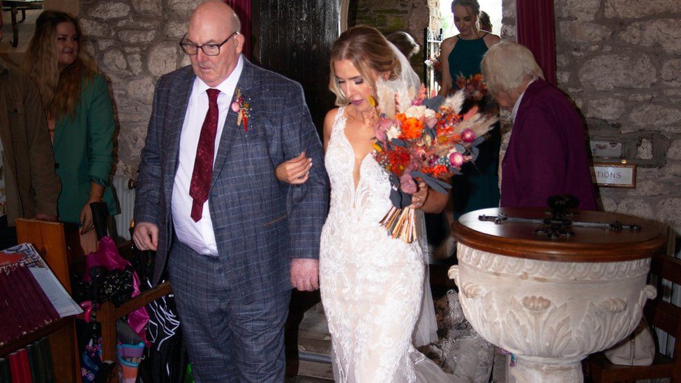 Roger and Jessie walking arm in arm down the aisle in a chapel