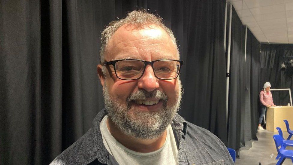 Man with grey hair and beard wearing glasses in a rehearsal studio