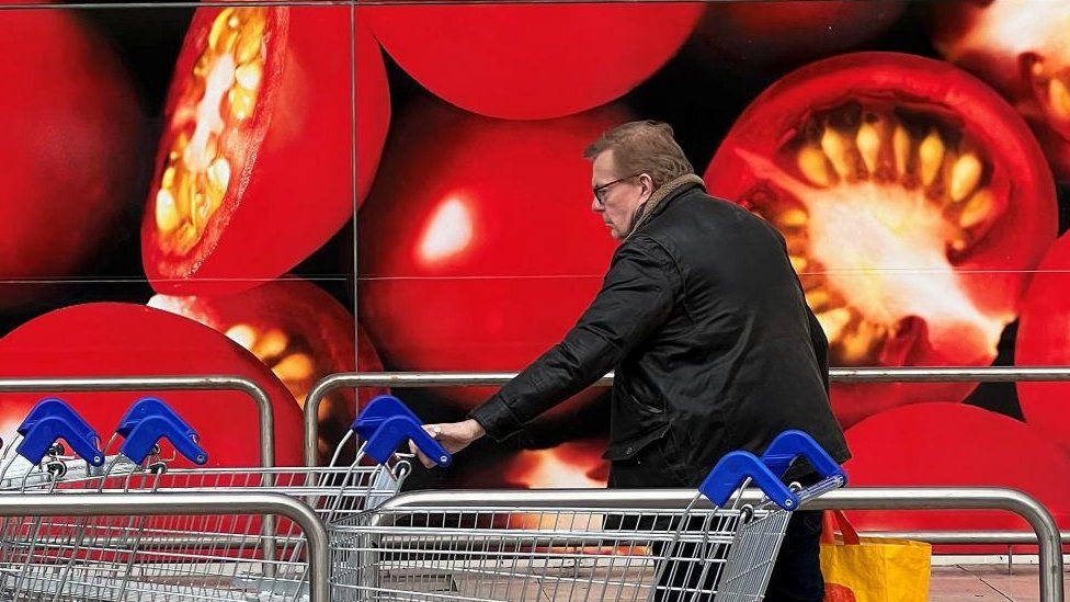 A man wheels a trolley in front of a big picture of tomatoes