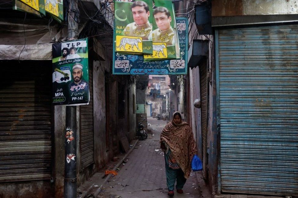 A woman walks past campaign posters a day ahead of the general election, at the Walled City in Lahore, Pakistan February 7, 2024.