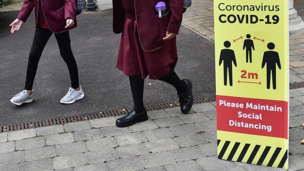 Secondary school pupils walk past social distancing sign