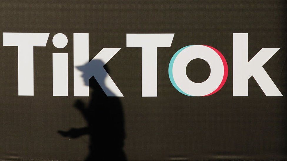 A young man holding a smartphone casts a shadow as he walks past an advertisement for social media company TikTok.