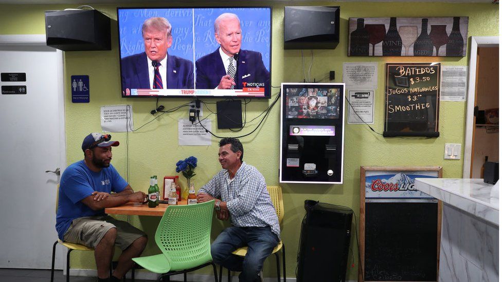 People sitting under screen of Trump Biden debate in Miami, Florida