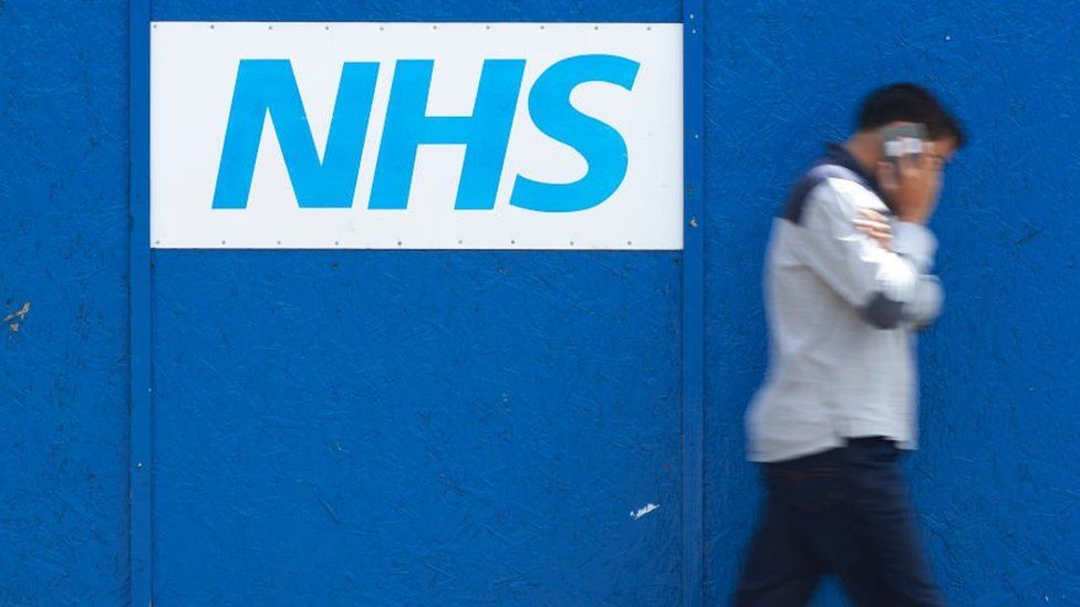 Picture of young adult walking past an NHS hospital
