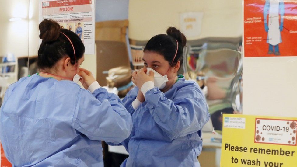 A healthcare worker placing a PPE mask on her face