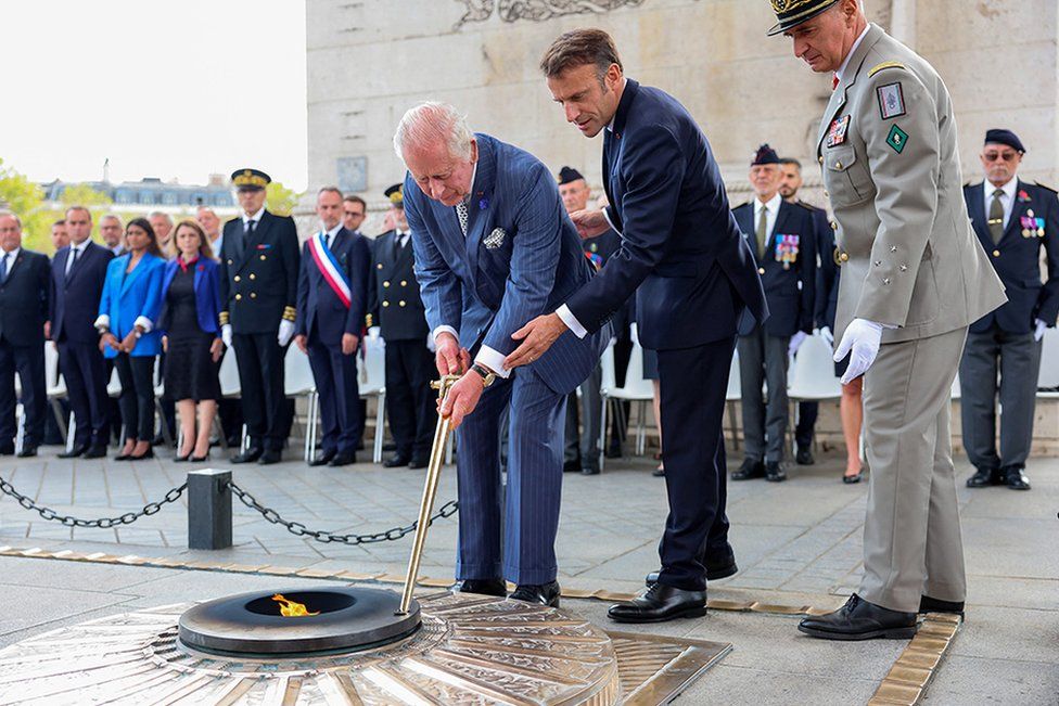 King Charles III performs the re-kindling of the eternal flame using the Comite de la Flamme passed to him by the President of France, Emmanuel Macron during a ceremonial welcome at The Arc De Triomphe