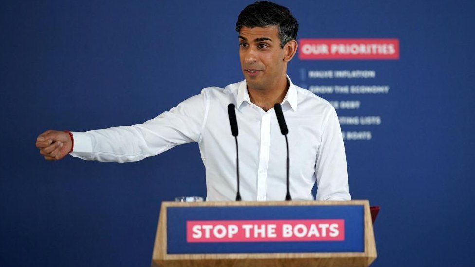 Rishi Sunak at a podium which reads "Stop the boats"